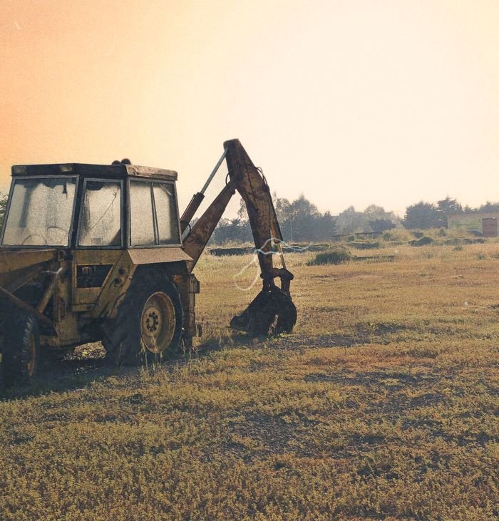 Rusty backhoe loader in an open grass field during sunrise in Babolsar, Iran.