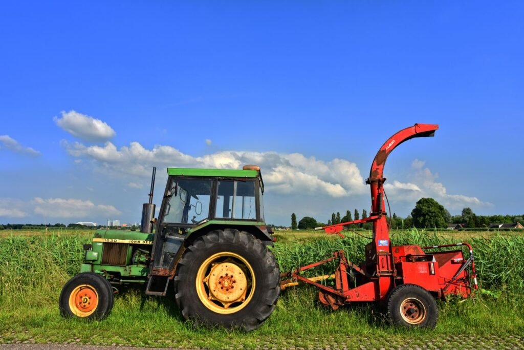 Green tractor and red harvester in a vibrant rural landscape under clear blue skies.