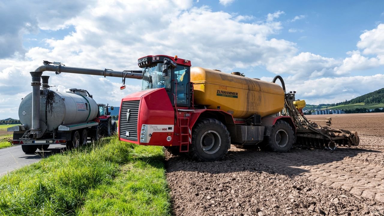 A red and yellow agricultural machine working in a rural field under a blue sky.